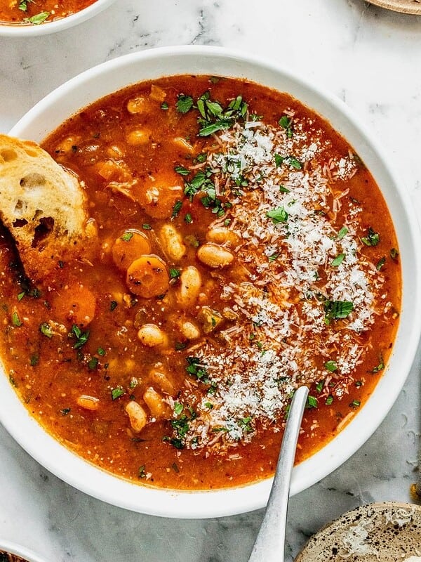 A bowl of fasolada Greek white bean soup garnished with parsley and cheese.