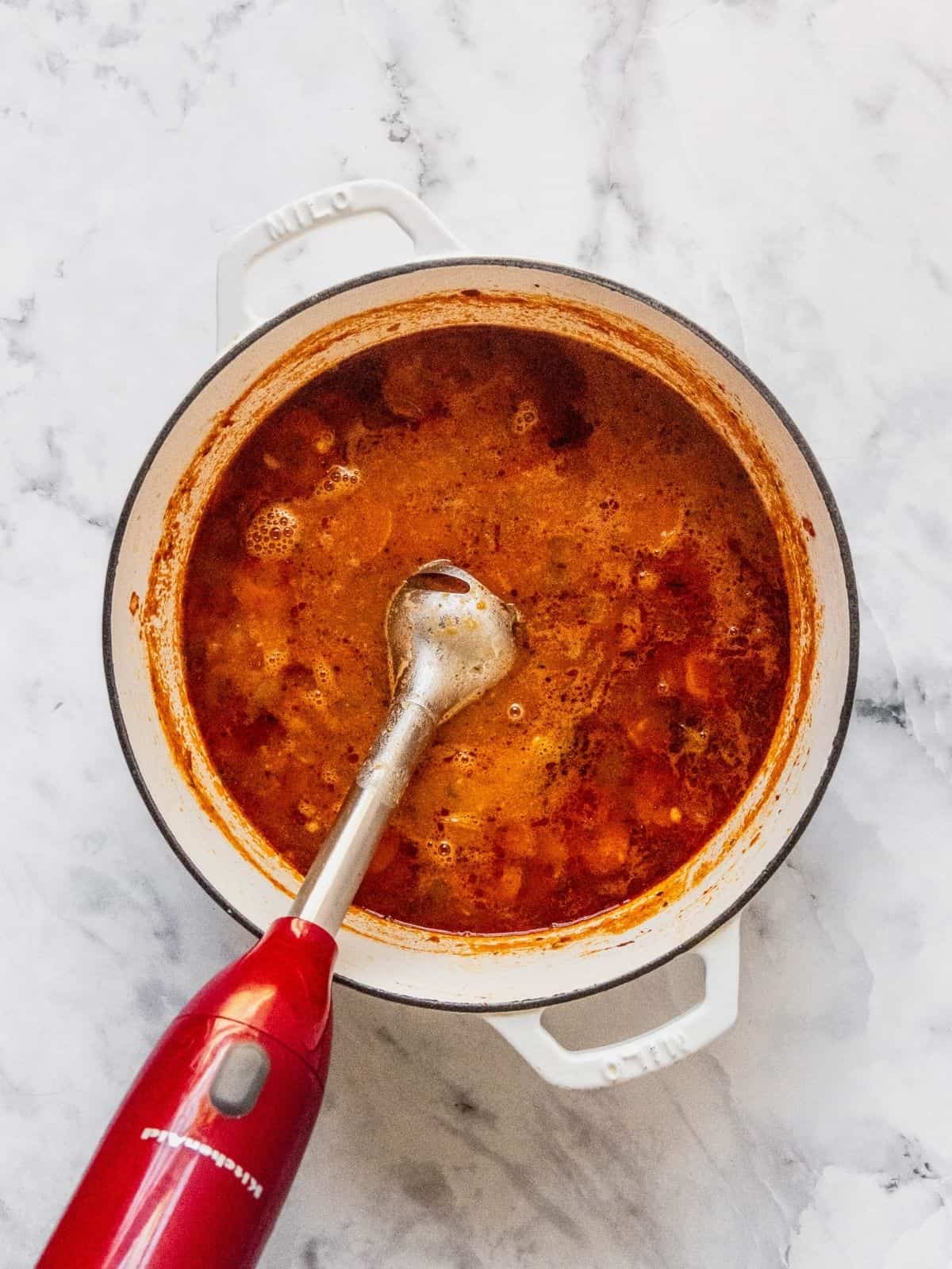 An immersion blender is used to puree some of the soup directly in the pot.