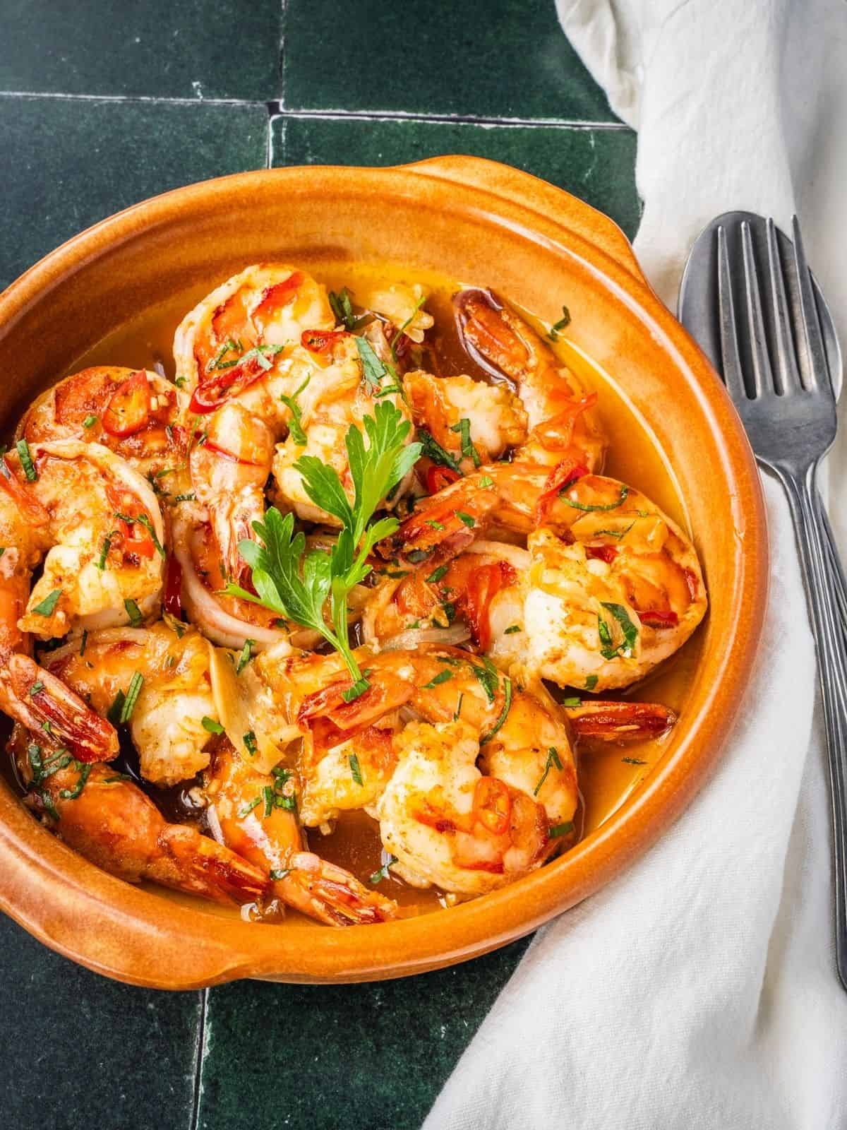 Gambas al ajillo, Spanish garlic shrimp, garnished with fresh parsley in a serving dish.