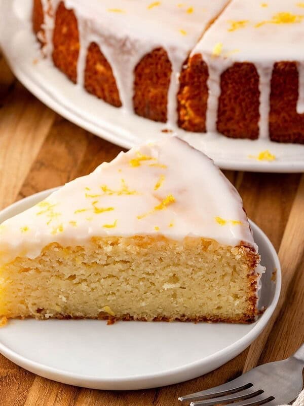 A slice of lemon ricotta cake on a plate, garnished with icing and lemon zest.