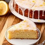 A slice of lemon ricotta cake on a plate, garnished with icing and lemon zest.