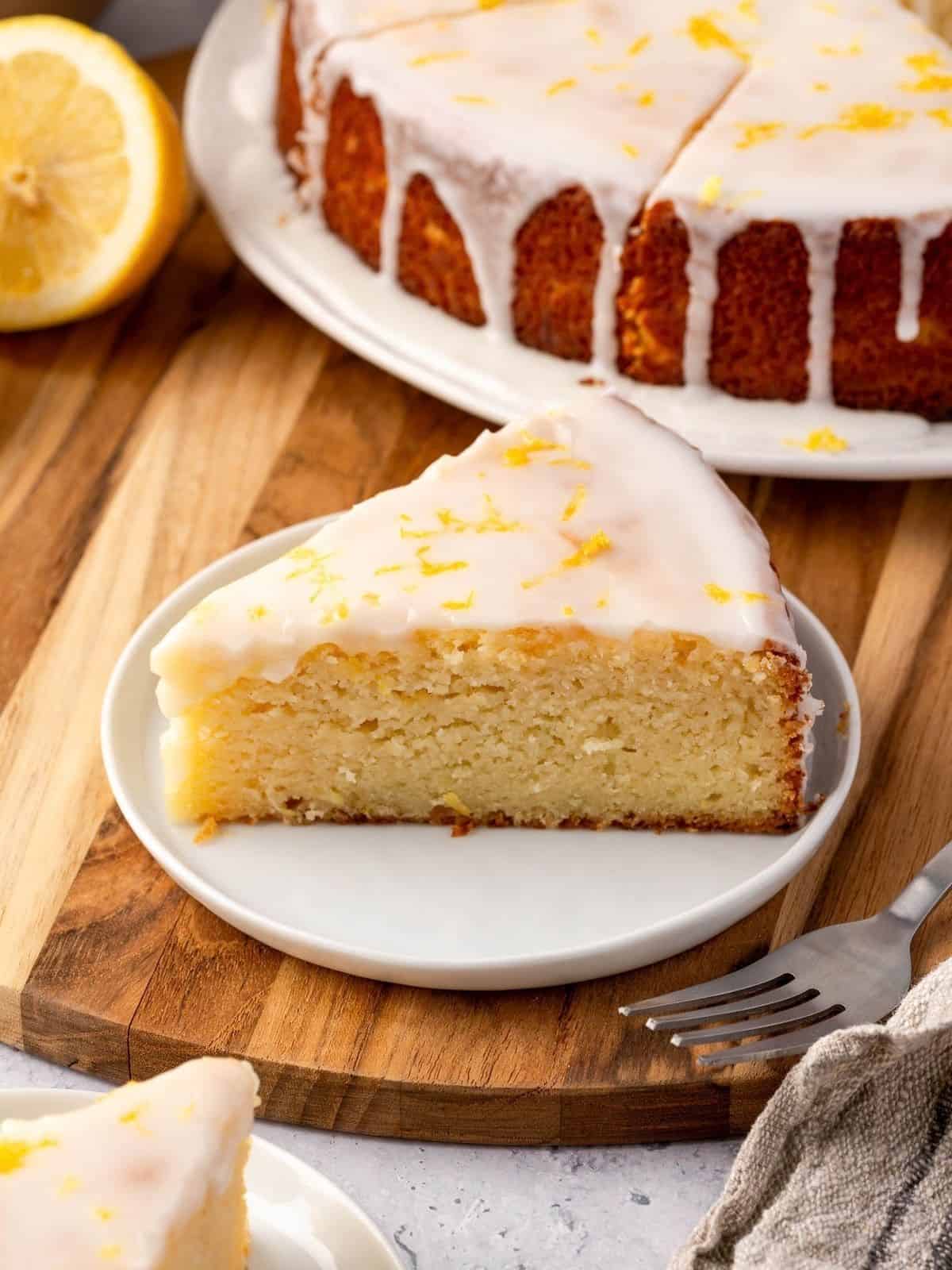 A slice of lemon ricotta cake on a plate, garnished with icing and lemon zest.