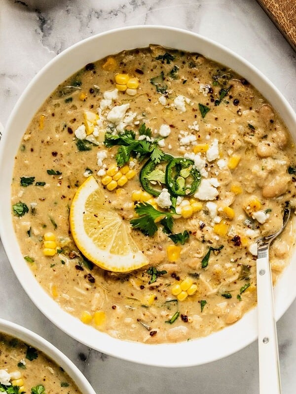 A bowl of Mediterranean white chicken chili, garnished with jalapeรฑos, feta, and a lemon wedge.