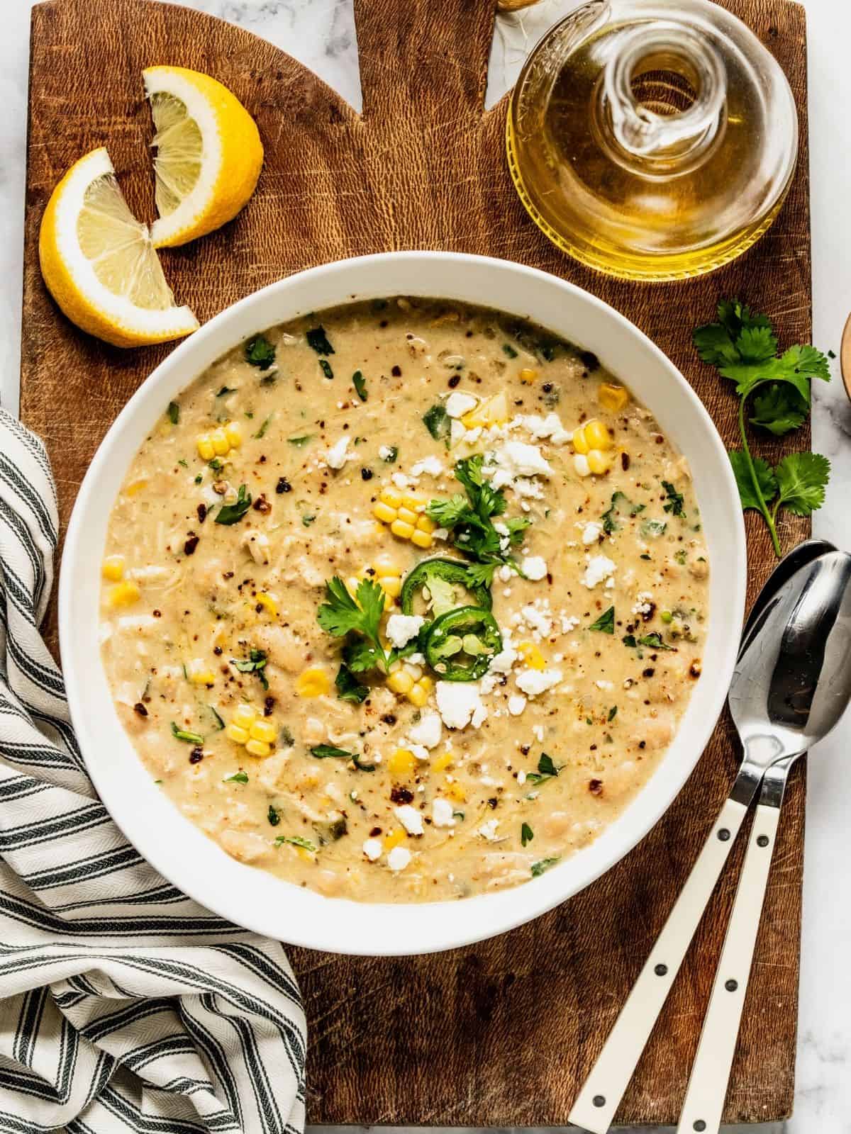 A bowl of Mediterranean white chicken chili, garnished with jalapeños, feta, and a lemon wedge.