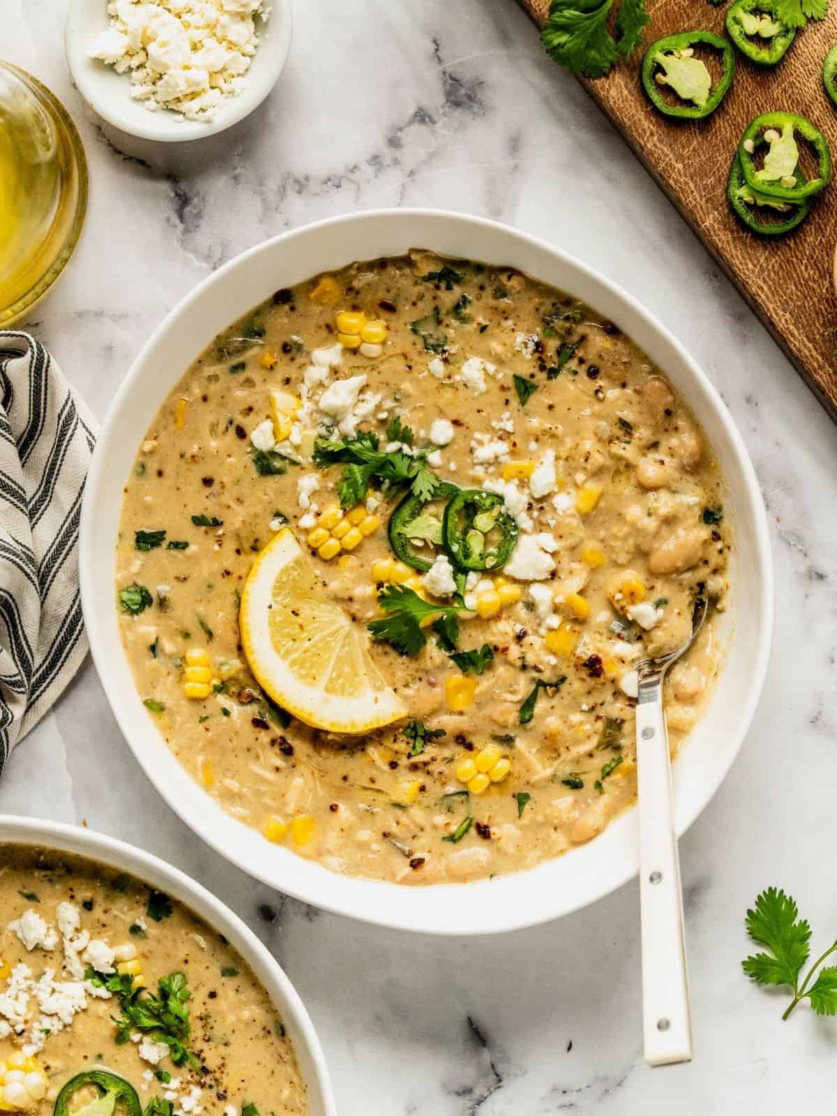 A bowl of Mediterranean white chicken chili, garnished with jalapeños, feta, and a lemon wedge.