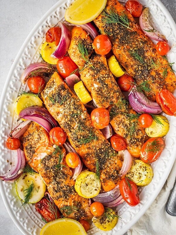 Za'atar salmon fillets on a serving platter with cherry tomatoes, squash, red onion, fresh dill and lemon wedges.