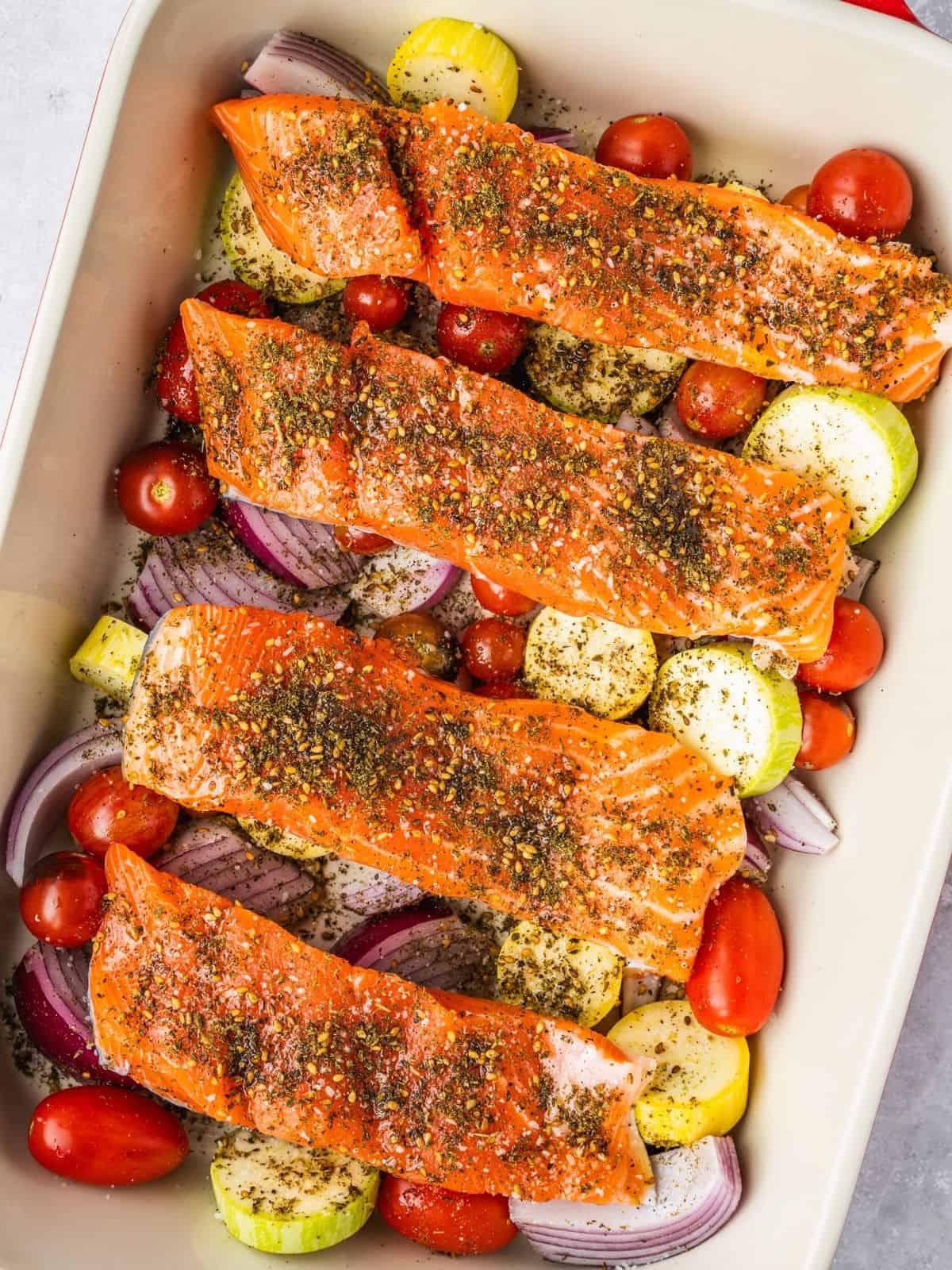 Za'atar seasoned salmon fillets placed over the seasoned vegetables in a baking tray.
