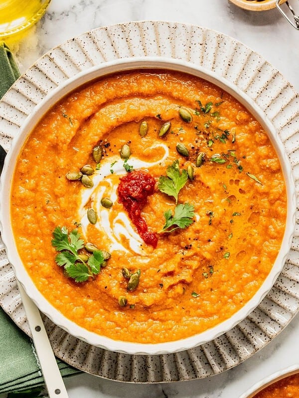 Toasted carrot soup with harissa and yogurt in a bowl garnished with cilantro and pumpkin seeds.