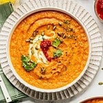 Toasted carrot soup with harissa and yogurt in a bowl garnished with cilantro and pumpkin seeds.