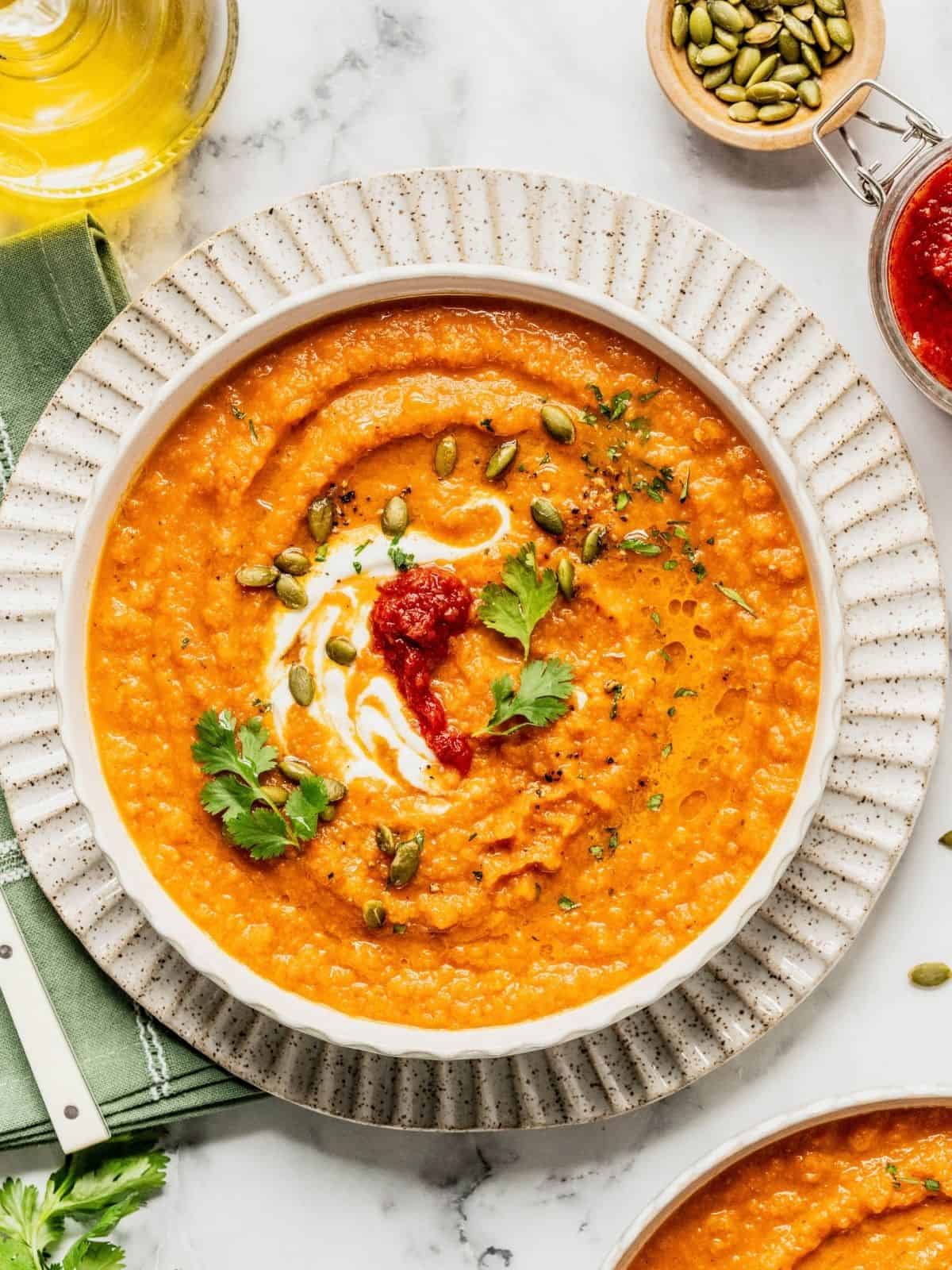 Toasted carrot soup with harissa and yogurt in a bowl garnished with cilantro and pumpkin seeds.