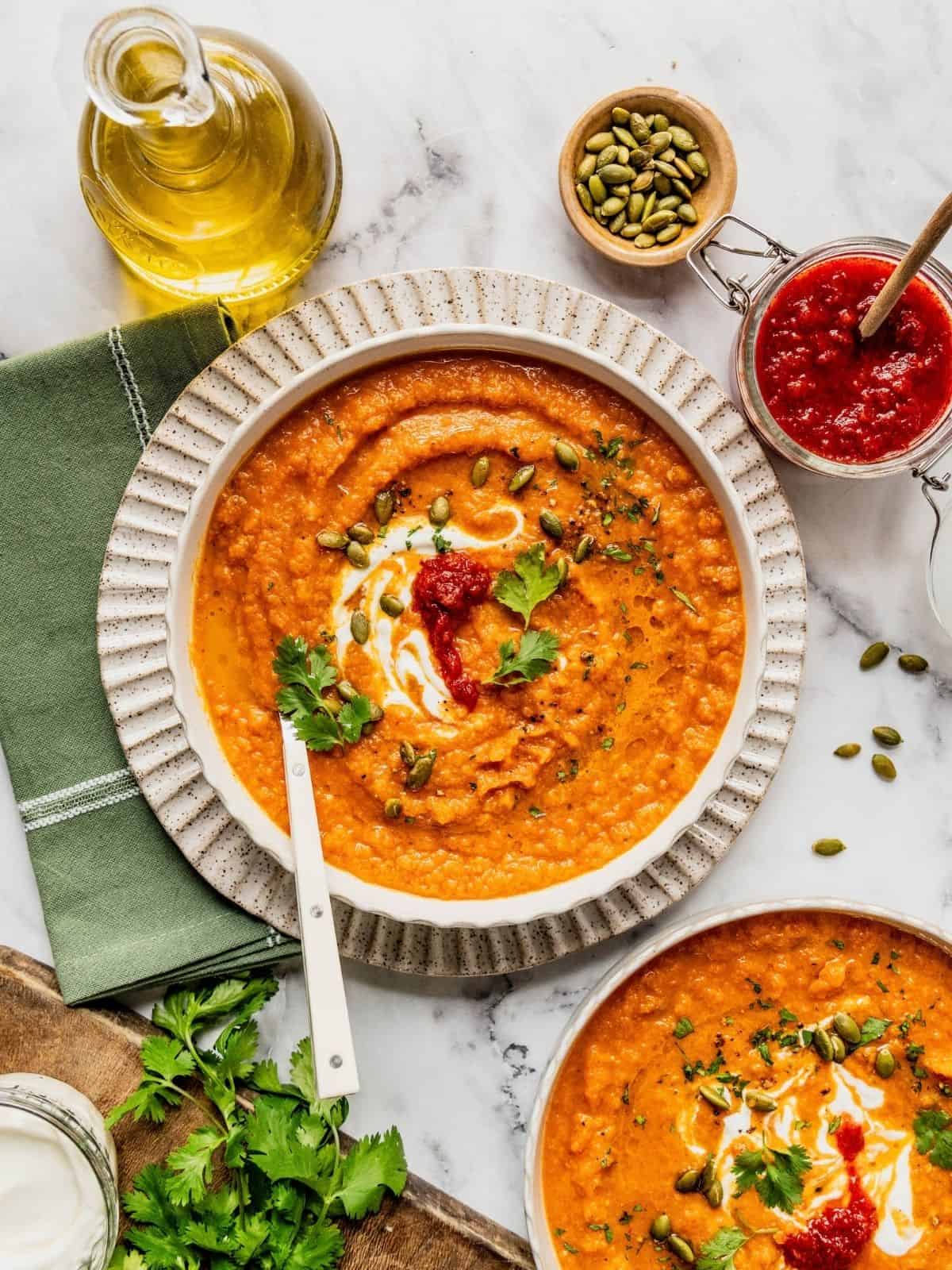 Toasted carrot soup with harissa and yogurt in a bowl garnished with cilantro and pumpkin seeds.
