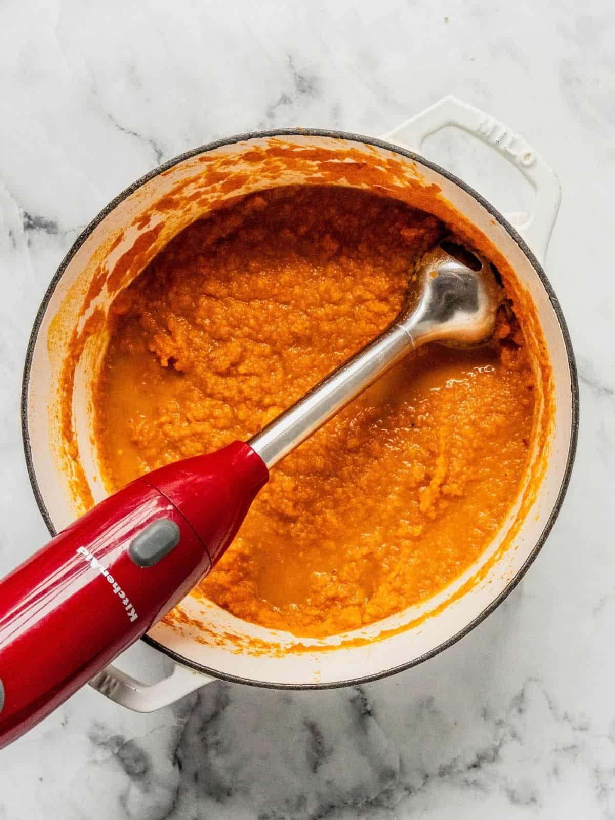 Immersion blender processing the carrot soup in a pot.