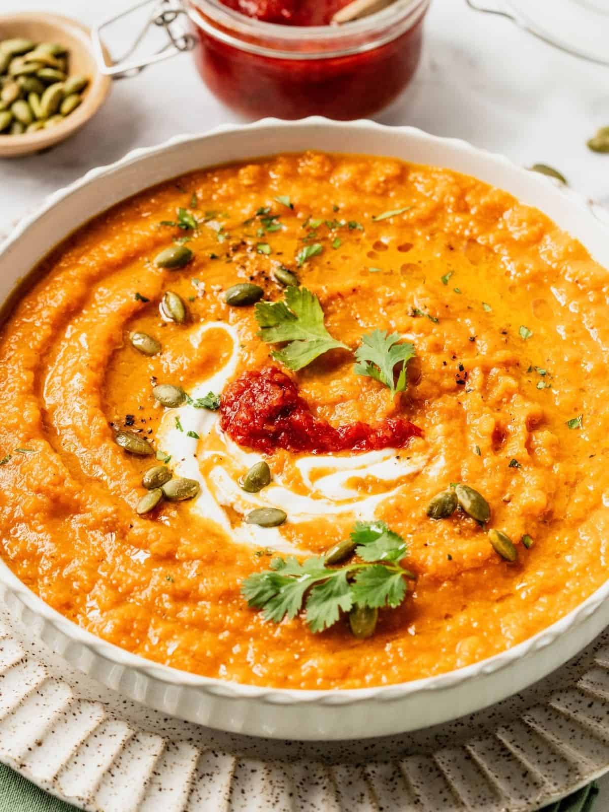 Toasted carrot soup with harissa and yogurt in a bowl garnished with cilantro and pumpkin seeds.