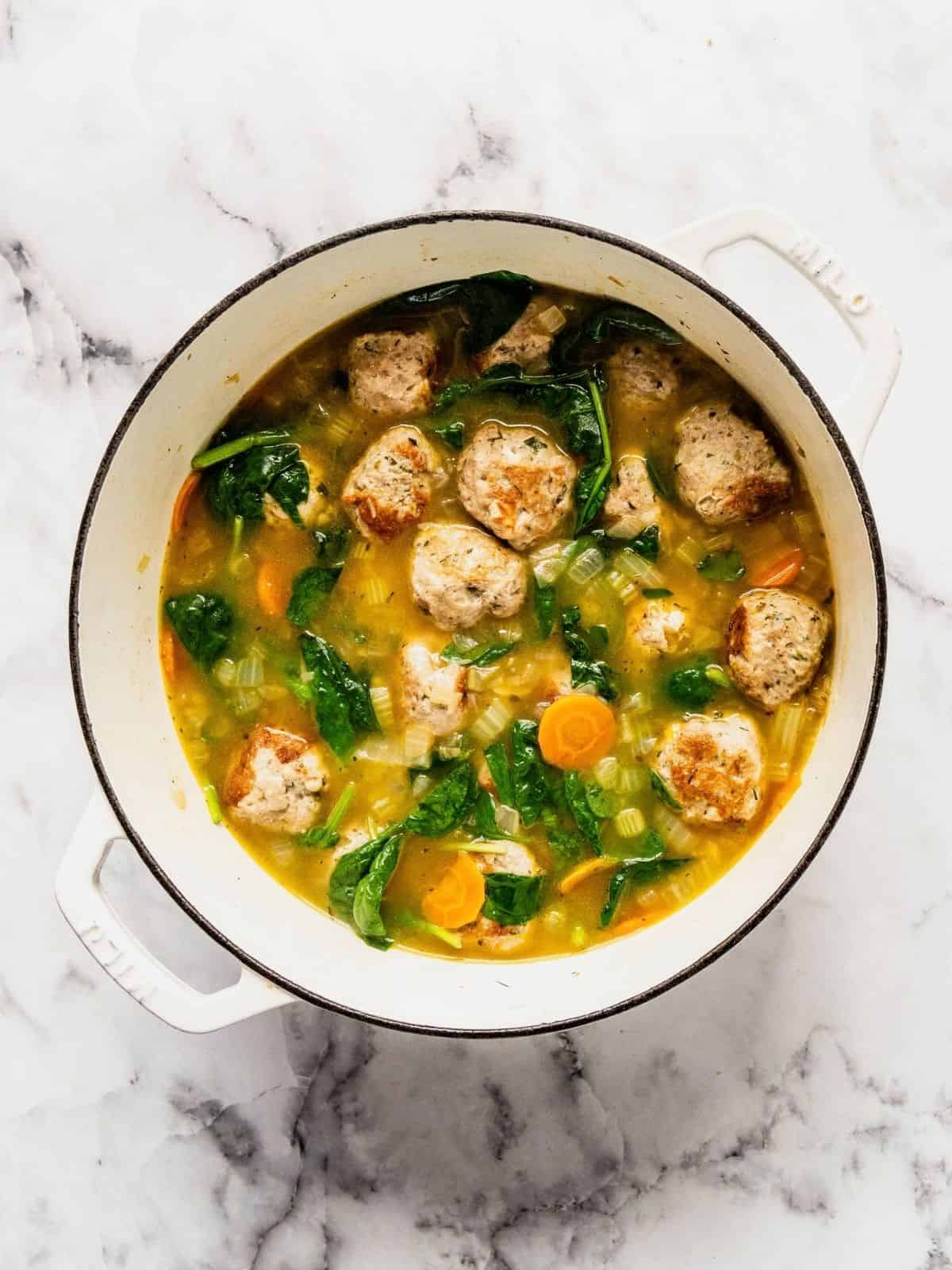 Soup pot with turkey meatballs, aromatics and wilted spinach.