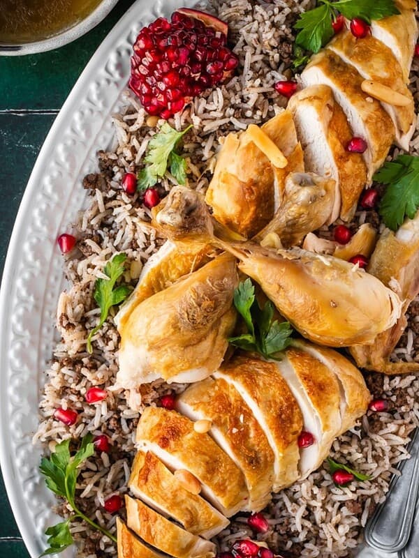 Sliced roast chicken over a bed of seasoned rice, garnished with parsley and pomegranate seeds.
