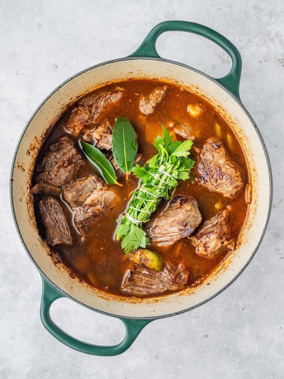 Pot with seared beef, aromatics, broth and herbs.