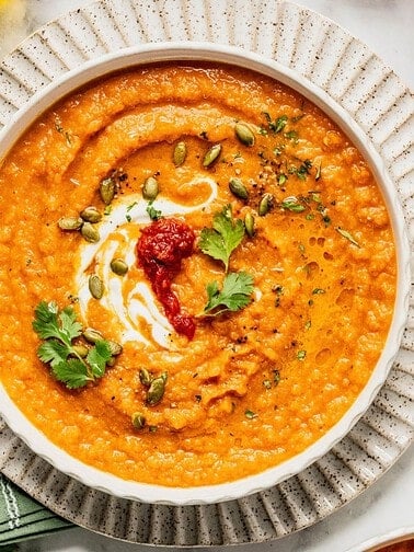 Roasted carrot soup with harissa and yogurt in a bowl garnished with cilantro and pumpkin seeds.