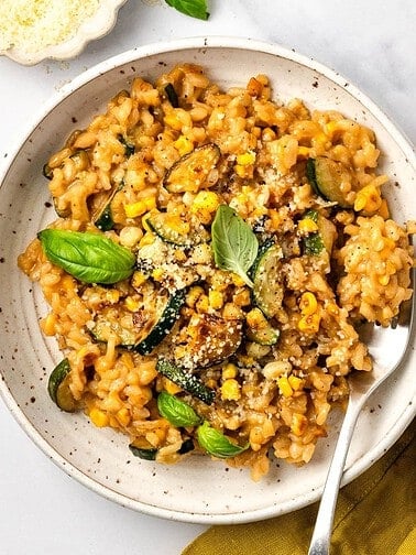 Corn zucchini risotto in a bowl garnished with basil.