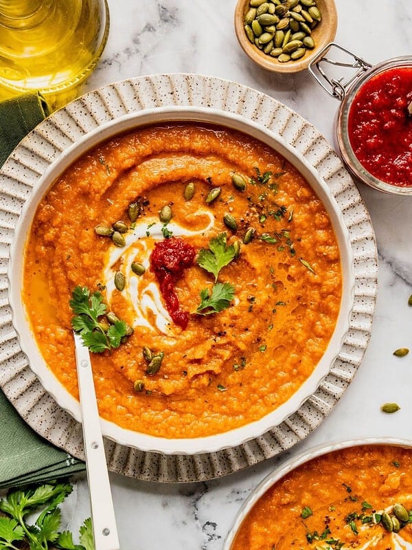Toasted carrot soup with harissa and yogurt in a bowl garnished with cilantro and pumpkin seeds.