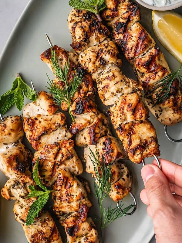 Chicken skewers on a platter with dill and lemon garnish.