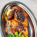Portuguese Shop Style grilled Piri Piri Chicken half on a platter with parsley and lemon.
